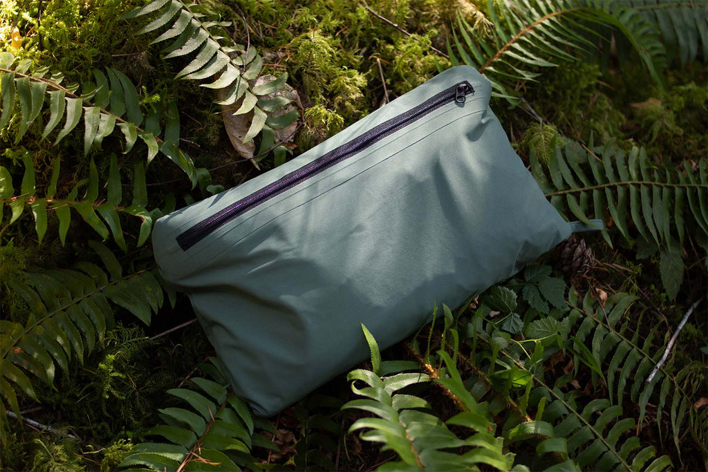 San Poncho waterproof, breathable, lightweight rain jacket, reversed into inner pocket to turn into a packable pouch on a bed of ferns